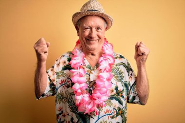 Sarı arka planda beyaz saçlı, son sınıf öğrencisi, yaz şapkası takıyor ve Hawaii kollarında gururla gülümseyen kol kaslarını gösteriyor. Fitness konsepti.