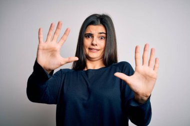 Genç, güzel esmer kadın beyaz arka plan üzerinde dikilmiş korku ifadesinden korkuyor ve dehşete düşmüş halde duruyor. El hareketlerini durdur, şok içinde bağır. Panik konsepti.