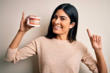 Diş protezi tutan genç ve güzel bir İspanyol dişçi bir fikir ya da soru karşısında şaşkın şaşkın gülümseyen bir yüz gösterdi.