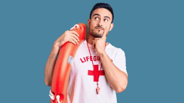 Cankurtaran üniforması giyen genç yakışıklı adam ciddi bir yüz ifadesi takınıyor eli çenesinde soruyu düşünüyor, kafa karıştırıcı bir fikir hakkında düşünceli. 