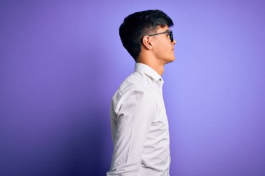 Tişört ve gözlük takan yakışıklı bir iş adamı mor arka planda kendine güvenen bir gülümsemeyle rahat bir görünüm takınıyor..