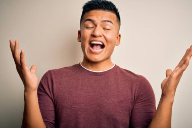 Genç, yakışıklı, latin bir adam izole edilmiş beyaz arka planda dikilmiş çılgın ve başarıyı kollarını kaldırıp heyecanla haykırarak kutluyor. Kazanan konsept