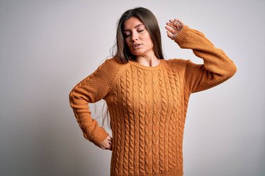 Mavi gözlü genç bir kadın beyaz arka planda dikiliyor, yorgun ve rahat, uykulu ve sabahın erken saatlerinde esniyor