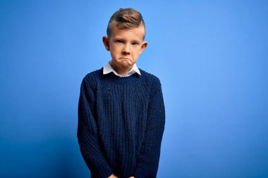 Mavi gözlü küçük beyaz çocuk mavi arka planda kışlık süveter giyiyor. Depresyonda ve sıkıntıdan endişe ediyor. Kızgın ve korkmuş. Üzücü ifade.