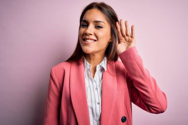 İzole edilmiş pembe arka planda duran ceketli genç ve güzel bir esmer kadın. Kulağı kulağında bir söylenti ya da dedikoduları dinliyor. Sağırlık kavramı.