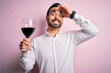 Sakallı, kırmızı şarap içen genç yakışıklı adam pembe arka planda, elleri başının üstünde, utanç ve şaşkınlık dolu, sinirli ve hayal kırıklığına uğramış bir halde. Hata için korku ve üzüntü.