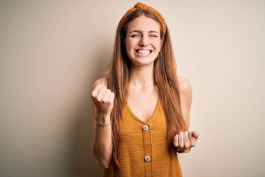 Sarı arka plan üzerine gündelik tişört ve diyabet giyen genç, güzel, kızıl saçlı bir kadın çok mutlu ve heyecanlı bir şekilde kollarını kaldırıp, gülümseyerek ve başarı için çığlık atarak zafer hareketi yapıyor. Kutlama konsepti.