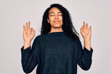 Beyaz arka planda sıradan bir süveter giyen genç Afro-Amerikan kıvırcık kadın rahatla ve gözleri kapalı parmaklarıyla meditasyon hareketi yaparken gülümse. Yoga konsepti.
