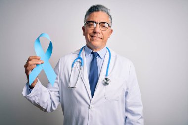 Orta yaşlı, yakışıklı, gri saçlı doktor elinde mavi kanser kurdelesi tutan, mutlu yüzlü, kendine güvenen bir gülümsemeyle dişlerini gösteren bir adam.