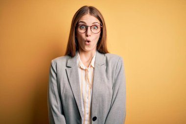 Ceket ve gözlük takan genç, güzel kızıl saçlı kadın sarı arka planda korkmuş ve şok olmuş..