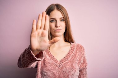 Genç, güzel, kızıl saçlı bir kadın pembe arka plan üzerine günlük süveter giyip avuç içiyle şarkı söylemeyi kesiyor. Yüzünde olumsuz ve ciddi bir jest olan uyarı ifadesi.