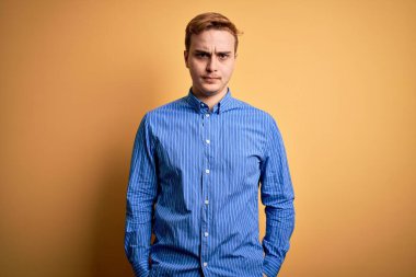 İzole edilmiş sarı arka plan şüphecisi ve gergin üzerine sıradan çizgili gömlek giyen genç, kızıl saçlı bir adam sorun yüzünden surat asıyor. Negatif kişi.