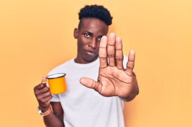 Genç Afrikalı Amerikalı adam elinde kahve ile dur işareti yapıyor. Ciddi ve kendinden emin bir ifadeyle, savunma jesti. 