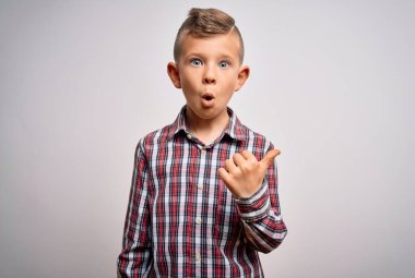 Mavi gözlü, zarif gömlekli, izole edilmiş arka planda duran küçük beyaz bir çocuk. El parmağı yanda, ağzı açık bir şekilde şaşkınlık içinde..