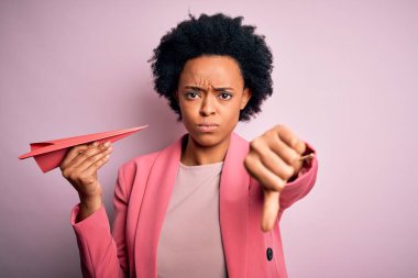 Genç, kıvırcık saçlı, kızgın yüzlü, pembe kâğıt uçak tutan Afro-Amerikalı bir kadın. Negatif işaretler, baş parmakları aşağıda, reddedilme kavramı.