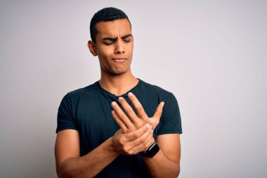 Young handsome african american man wearing casual t-shirt standing over white background Suffering pain on hands and fingers, arthritis inflammation clipart