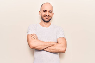 Genç, kel, rahat tişört giyen, kollarını kavuşturup kameraya bakan mutlu yüzlü bir adam. pozitif kişi. 