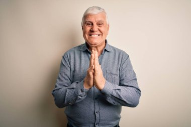 Kıdemli yakışıklı beyaz gömlekli adam izole edilmiş beyaz arka planda duruyor ellerini birleştirip af diliyor kendinden emin bir şekilde gülümsüyor..
