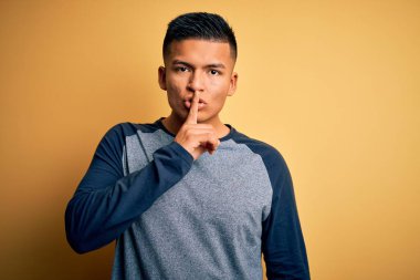 Sarı arka plan üzerinde sıradan tişörtler giyen genç ve yakışıklı Latin adam sessiz olmak istiyor. Sessizlik ve gizli konsept.