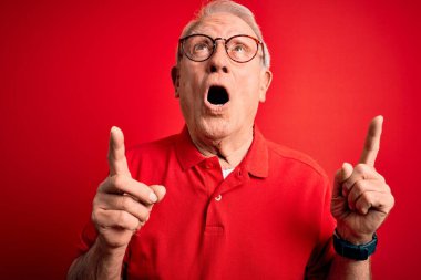 Gri saçlı, gözlüklü ve kırmızı arka planda sıradan tişörtlü yaşlı adam şaşırmış ve şaşırmıştı. Parmaklarıyla işaret ediyor ve kollarını kaldırıyordu..