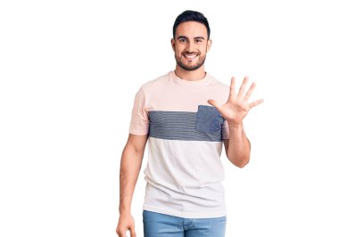 Gündelik kıyafetler giyen genç yakışıklı adam beş numarayı gösterip işaret ederken kendinden emin ve mutlu bir şekilde gülümsüyor.. 