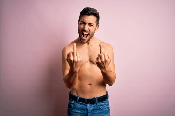 Young handsome strong man with beard shirtless standing over isolated pink background Showing middle finger doing fuck you bad expression, provocation and rude attitude. Screaming excited