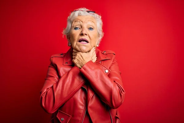 Senior beautiful grey-haired woman wearing casual red jacket and sunglasses shouting and suffocate because painful strangle. Health problem. Asphyxiate and suicide concept.