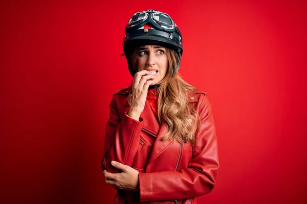 赤の背景に元ヘルメットを身に着けている若い美しいブルネットのオートバイの女性は 口の上で爪をかむ上で手でストレスと神経を見ています 不安の問題 — ストック写真