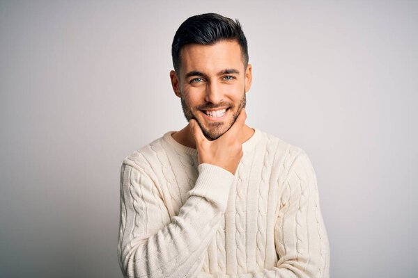 Young handsome man wearing casual sweater standing over isolated white background looking confident at the camera smiling with crossed arms and hand raised on chin. Thinking positive.