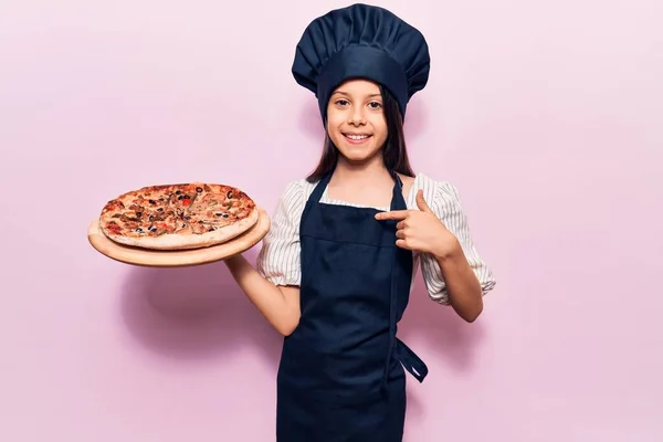 Красивая Девочка Мундире Держит Итальянскую Пиццу Указывая Пальцем Себя Улыбаясь — стоковое фото