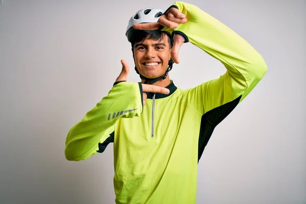 Young handsome cyclist man wearing security bike helmet over isolated white background smiling making frame with hands and fingers with happy face. Creativity and photography concept.
