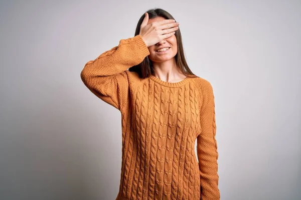 Young beautiful woman with blue eyes wearing casual sweater standing over white background smiling and laughing with hand on face covering eyes for surprise. Blind concept.