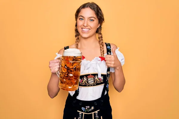 美しいブロンドドイツ人女性で青い目を身に着けています10月祭のドレスビールの瓶を飲みます幸せな大きな笑顔でOkサインをします 指で親指アップ 優れたサイン — ストック写真