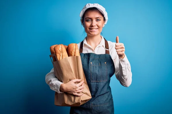 年轻美丽的面包师女人 蓝眼睛 手握纸袋 面带微笑快乐做手势 用手指竖起大拇指 很好的标志 — 图库照片