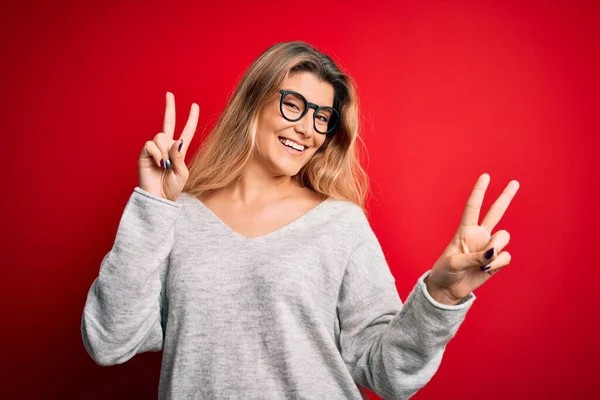 Jovem Mulher Loira Bonita Vestindo Suéter Óculos Sobre Fundo Vermelho — Fotografia de Stock