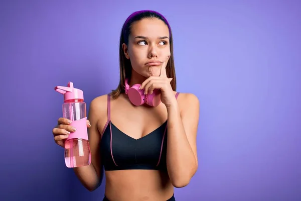 漂亮的女运动员用耳机做运动 喝了一瓶水让人神清气爽严肃的脸在想问题 非常迷惑的想法 — 图库照片