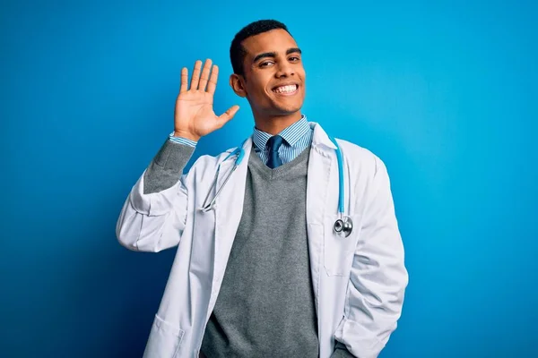 青い背景にコートと聴診器を身に着けているハンサムなアフリカ系アメリカ人医師こんにちは幸せと笑顔 優しい歓迎ジェスチャー — ストック写真