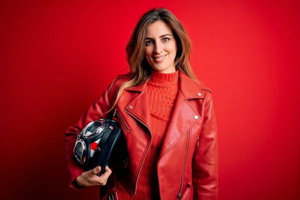 美しいブルネットのオートバイの女性は幸せな顔をして立っていると自信を持って笑顔で笑みを浮かべてオートバイのヘルメットを保持赤いジャケットを着て歯を示す — ストック写真