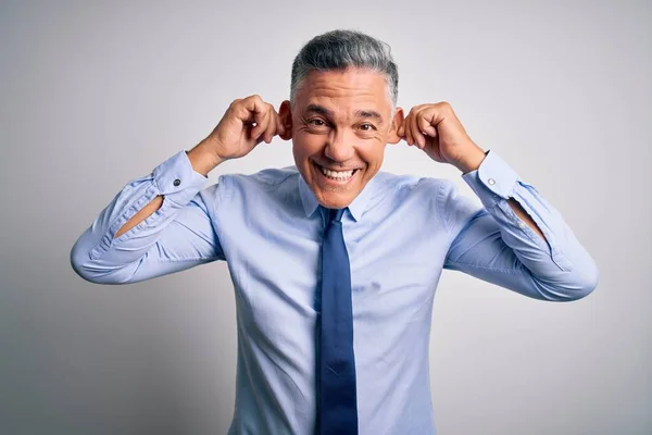 Middle age handsome grey-haired business man wearing elegant shirt and tie Smiling pulling ears with fingers, funny gesture. Audition problem
