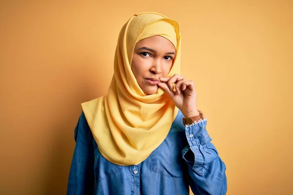 黄色い背景の口と唇の上にアラブの伝統的なヒジャーブを身に着けている巻き毛の美しい女性は指でジップとしてシャットダウンします 秘密裏に黙ってタブーを語る — ストック写真