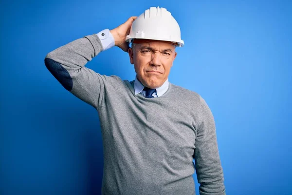 青い背景の上に安全ヘルメットを身に着けている中世のハンサムな白髪のエンジニアの人は混乱し 質問について疑問に思う 疑いもなく 頭の上で手で考えて 包括的概念 — ストック写真