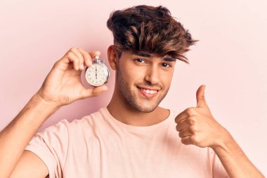 Kronometre tutan genç İspanyol adam mutlu ve pozitif gülümsüyor, başparmağıyla mükemmel ve onay işareti yapıyor. 