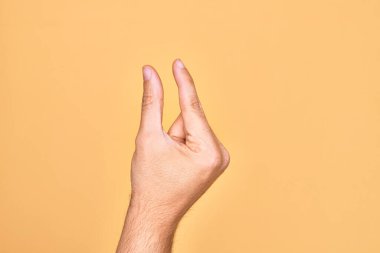 İzole edilmiş sarı arka plan üzerinde parmaklarını gösteren beyaz bir adamın eli. Görünmez bir şeyi alıp, parmaklarıyla uzayı gösteren bir nesneyi tutuyor.