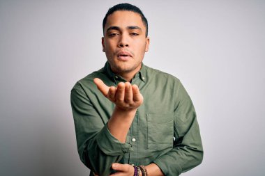 İzole edilmiş beyaz arka plan üzerinde dikilen Brezilyalı genç bir adam havayla öpüşürken kameraya bakıyor. Güzel ve seksi. Aşk ifadesi.