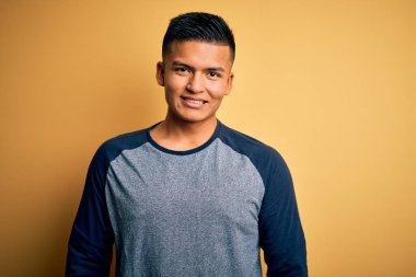 Sarı arka planda mutlu ve havalı bir gülümsemeyle dikilen, gündelik tişört giyen genç, yakışıklı latin adam. Şanslı kişi..