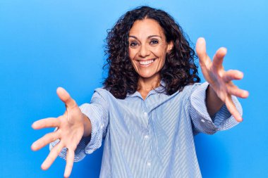 Orta yaşlı, güzel bir kadın. Sıradan bir tişört giymiş kameraya bakıyor. Sarılmak için kollarını açmış gülümsüyor. Mutluluğu kucaklayan neşeli bir ifade.. 