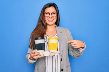 Genç Latin asıllı stajyer iş kadını elinde mavi arka planda kahveyle mutlu bir şekilde işaret ediyor.
