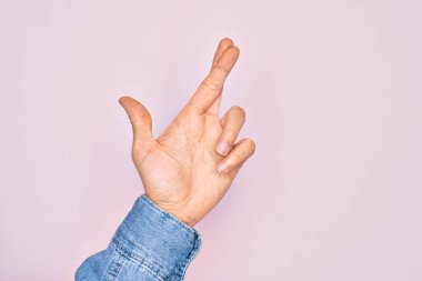 İzole edilmiş pembe arka plan üzerinde parmaklarını gösteren beyaz bir gencin eli. Parmakları çapraz, batıl inançlar ve şanslı bir jest, şanslı ve umut dolu bir ifade.