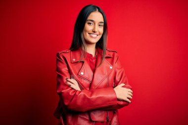 Genç, güzel, esmer, günlük ceket giyen, izole edilmiş kırmızı arka planda duran, kollarını kavuşturup kameraya gülümseyen bir kadın. Pozitif kişi.