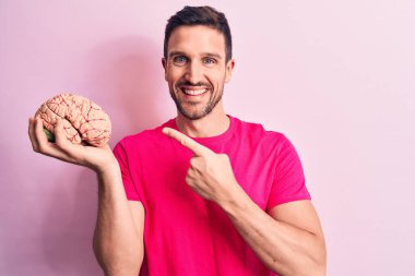 Genç ve yakışıklı bir adam, beyni soyutlanmış pembe arka planda tutan ve mutlu bir şekilde elini ve parmağını gösteren özenli bir anı istiyor.